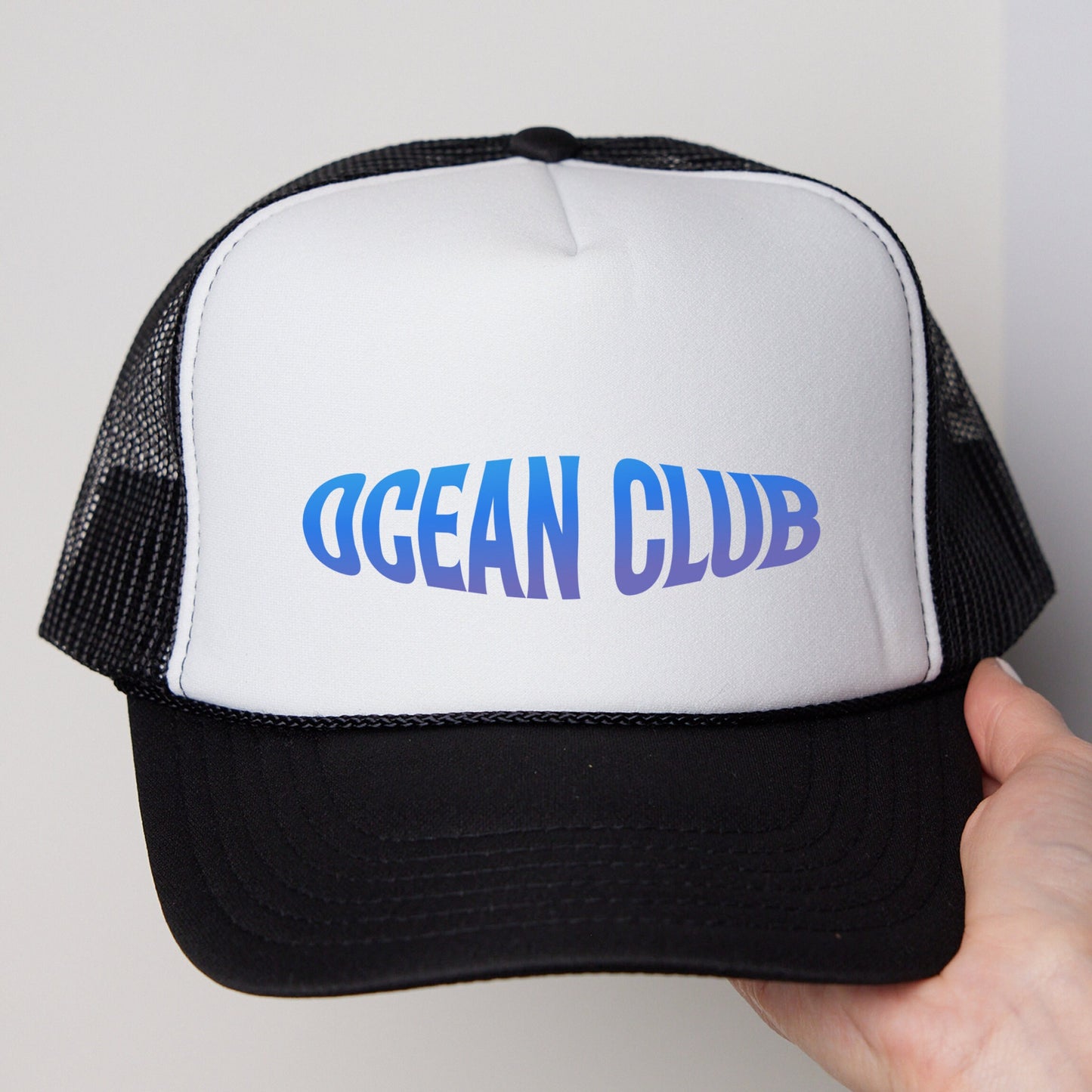 a hand holding a white and black ocean club trucker hat