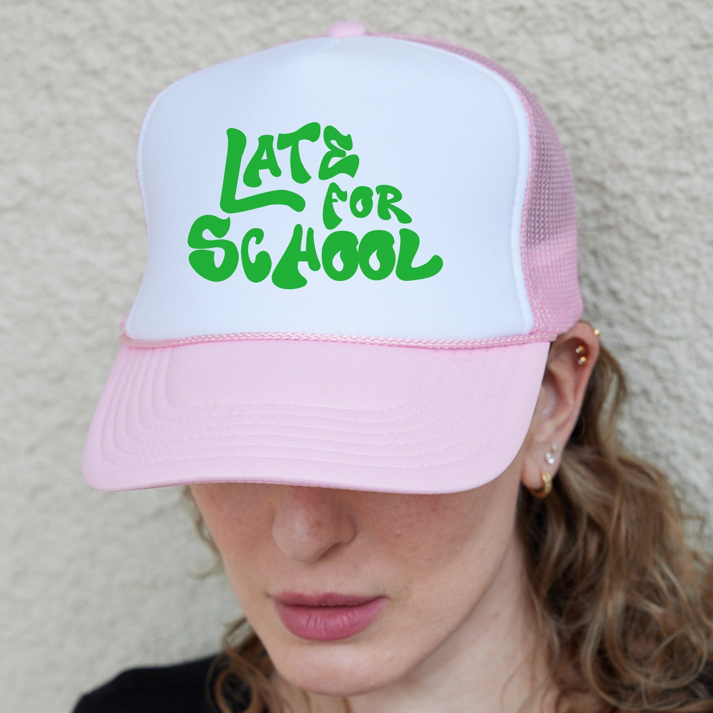 a woman wearing a pink and white hat with the words late for school on it