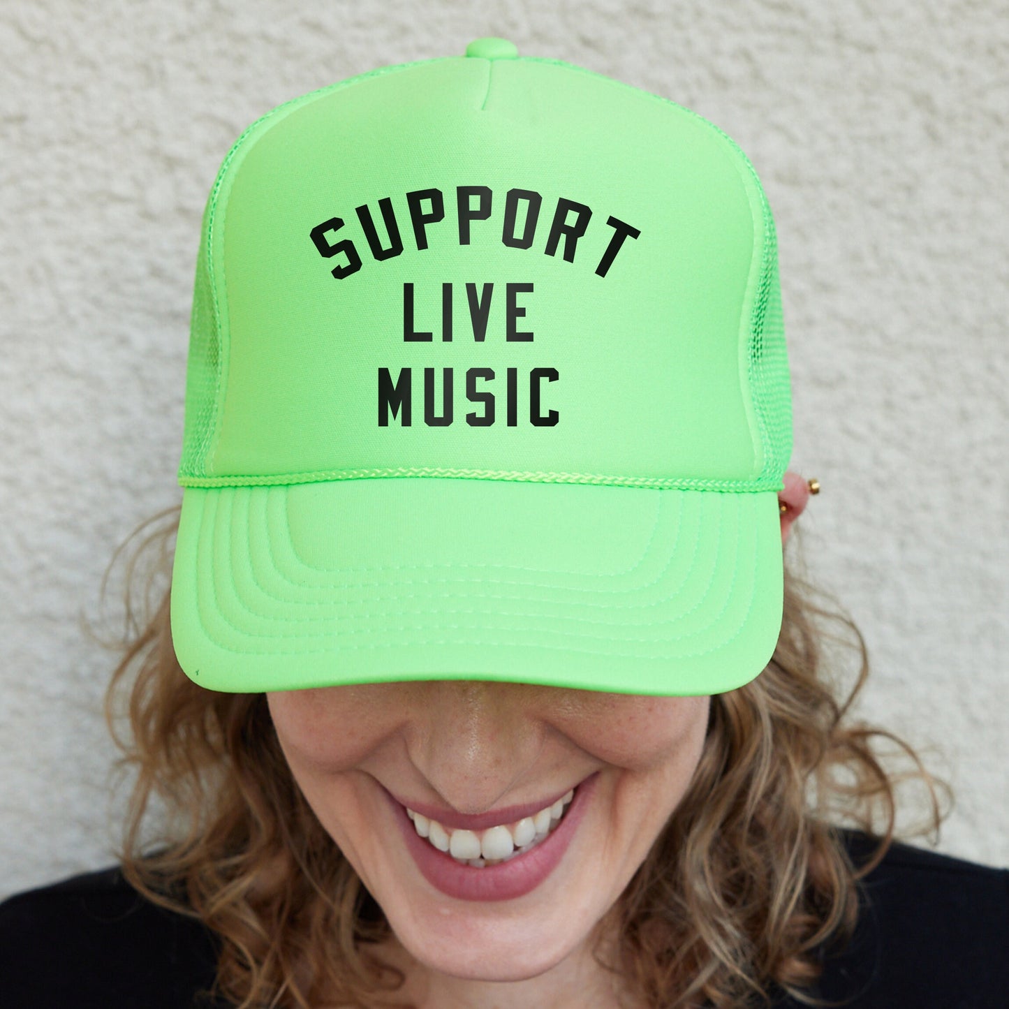 a woman wearing a neon green trucker hat that says support live music