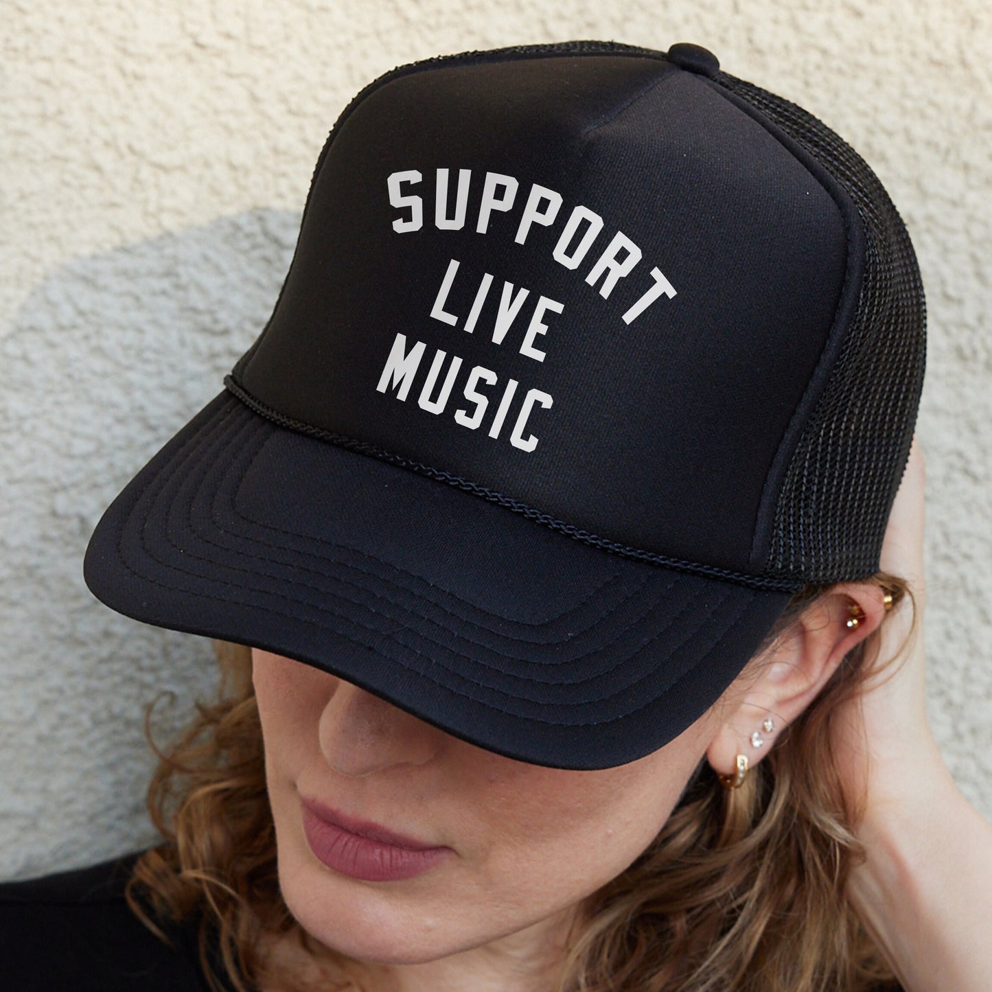 a woman wearing a black trucker hat that says support live music