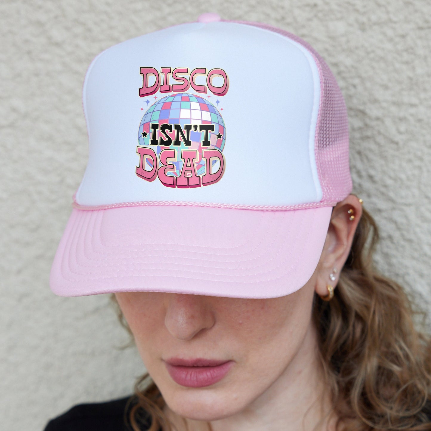 a woman wearing a pink and white trucker hat with disco isn't dead