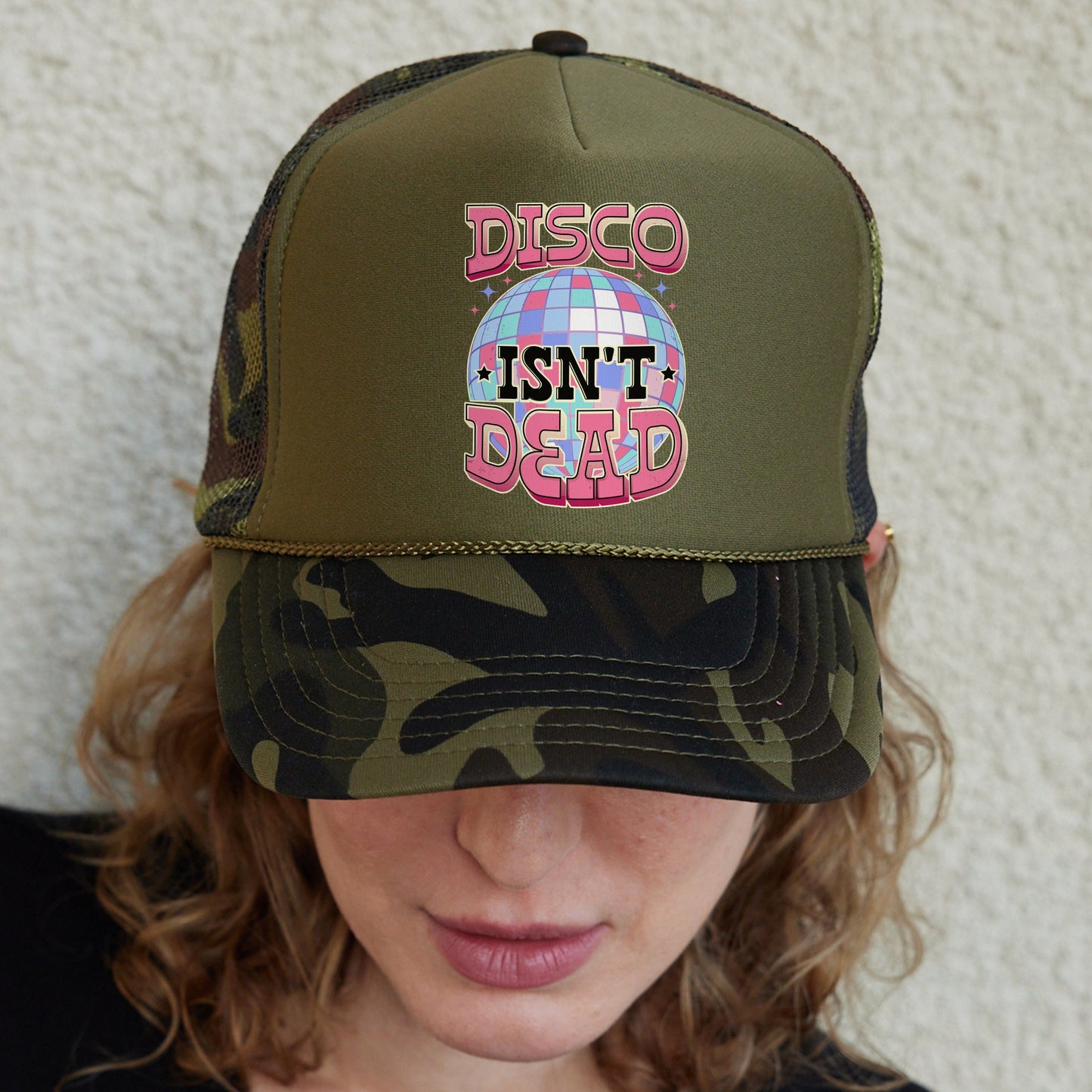 a woman wearing a green trucker hat with disco isn't dead on it