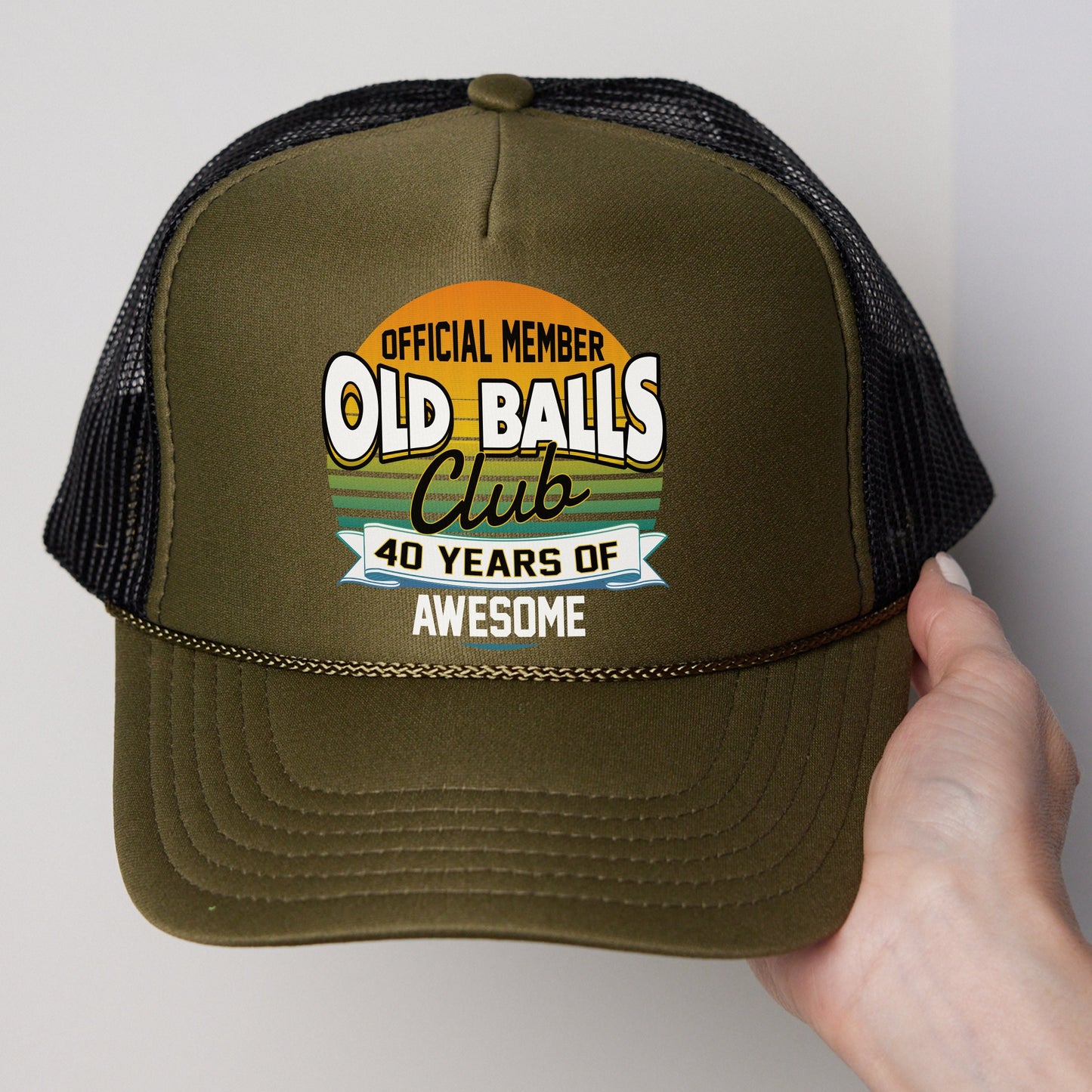 a person holding a trucker hat that says old balls club 40 years of awesome