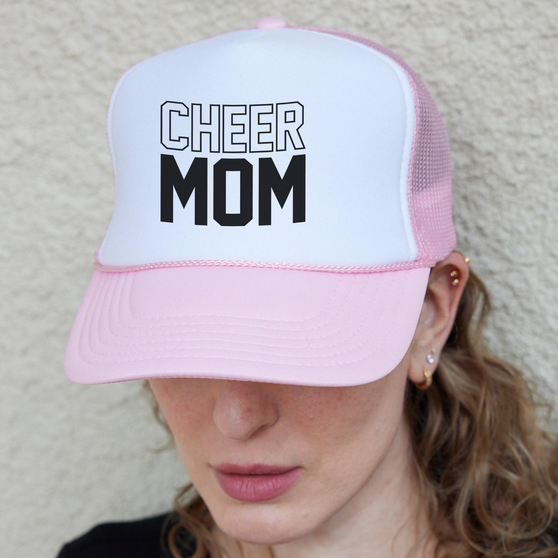 a woman wearing a pink and white hat with the word cheer mom on it