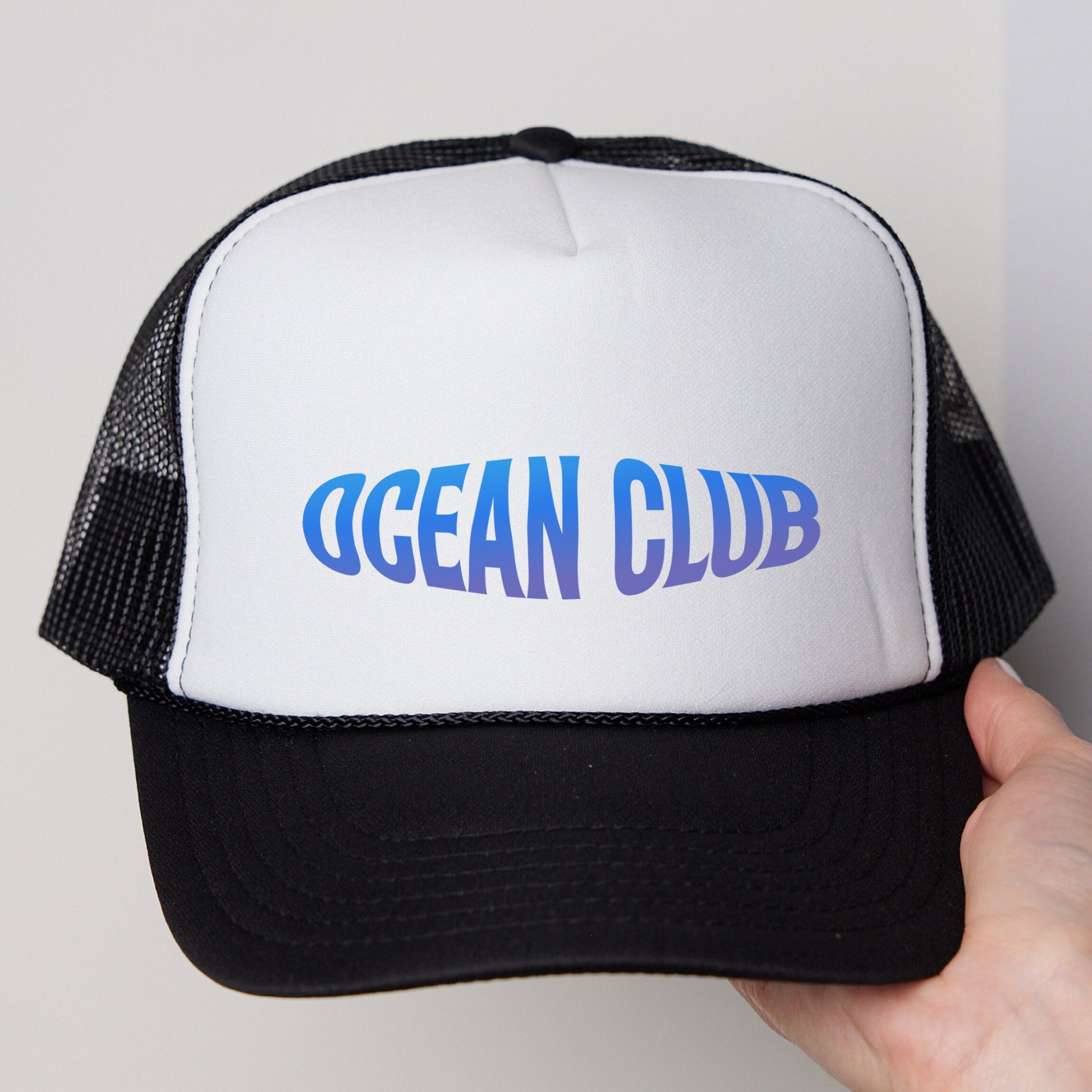 a hand holding a white and black ocean club trucker hat