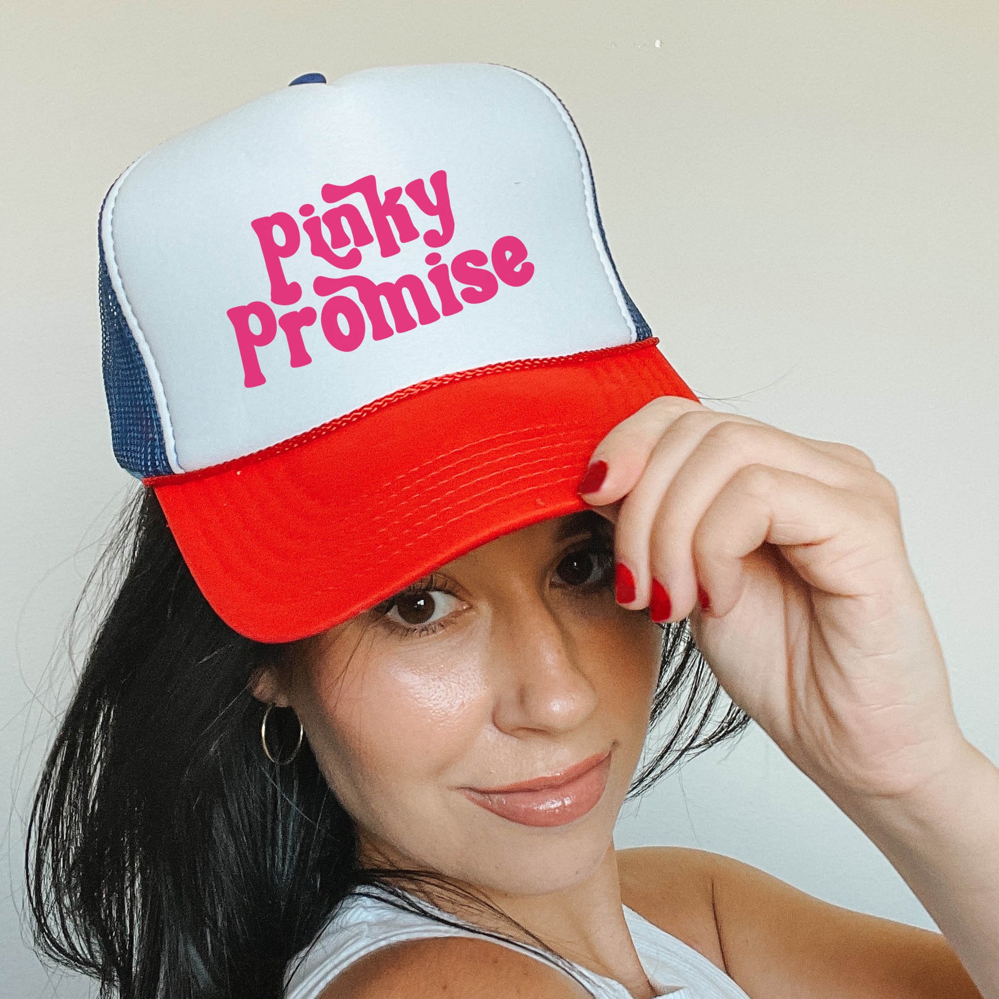 a woman in a white tank top and a red and blue trucker hat