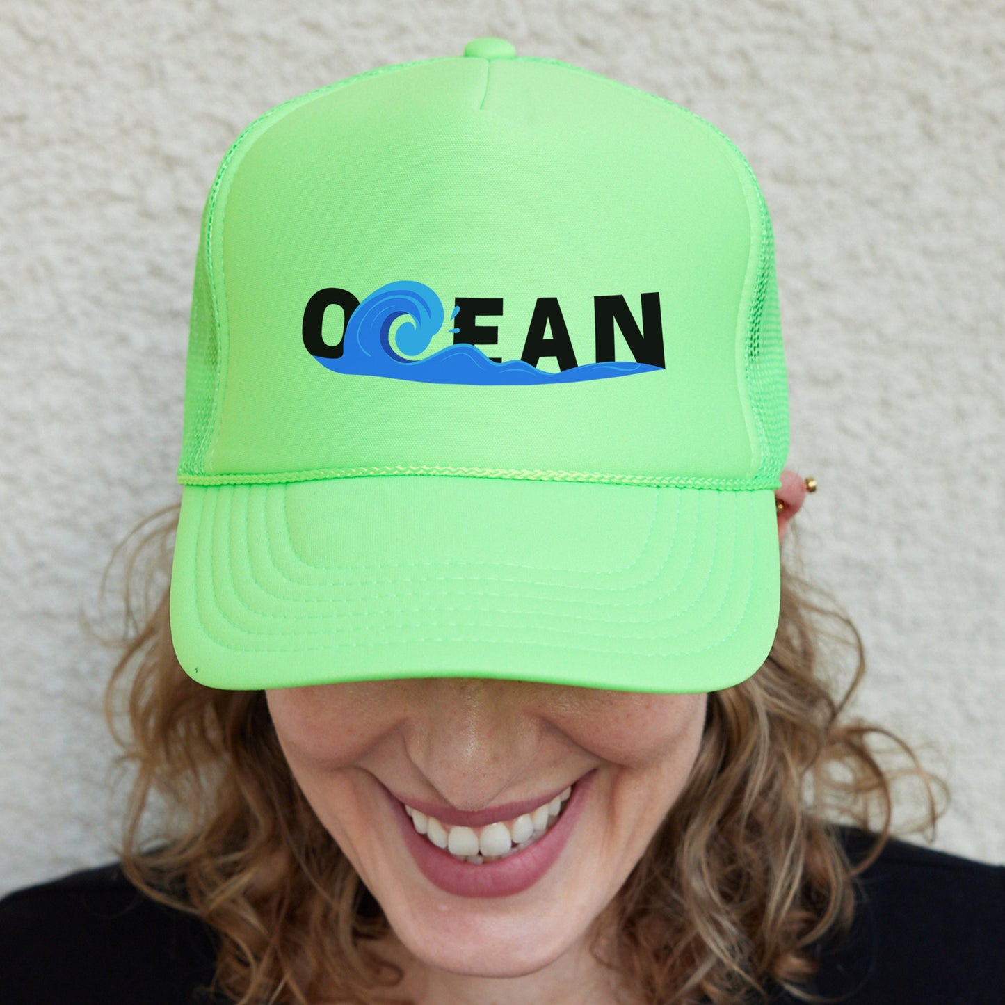 a smiling woman wearing a neon green ocean trucker hat