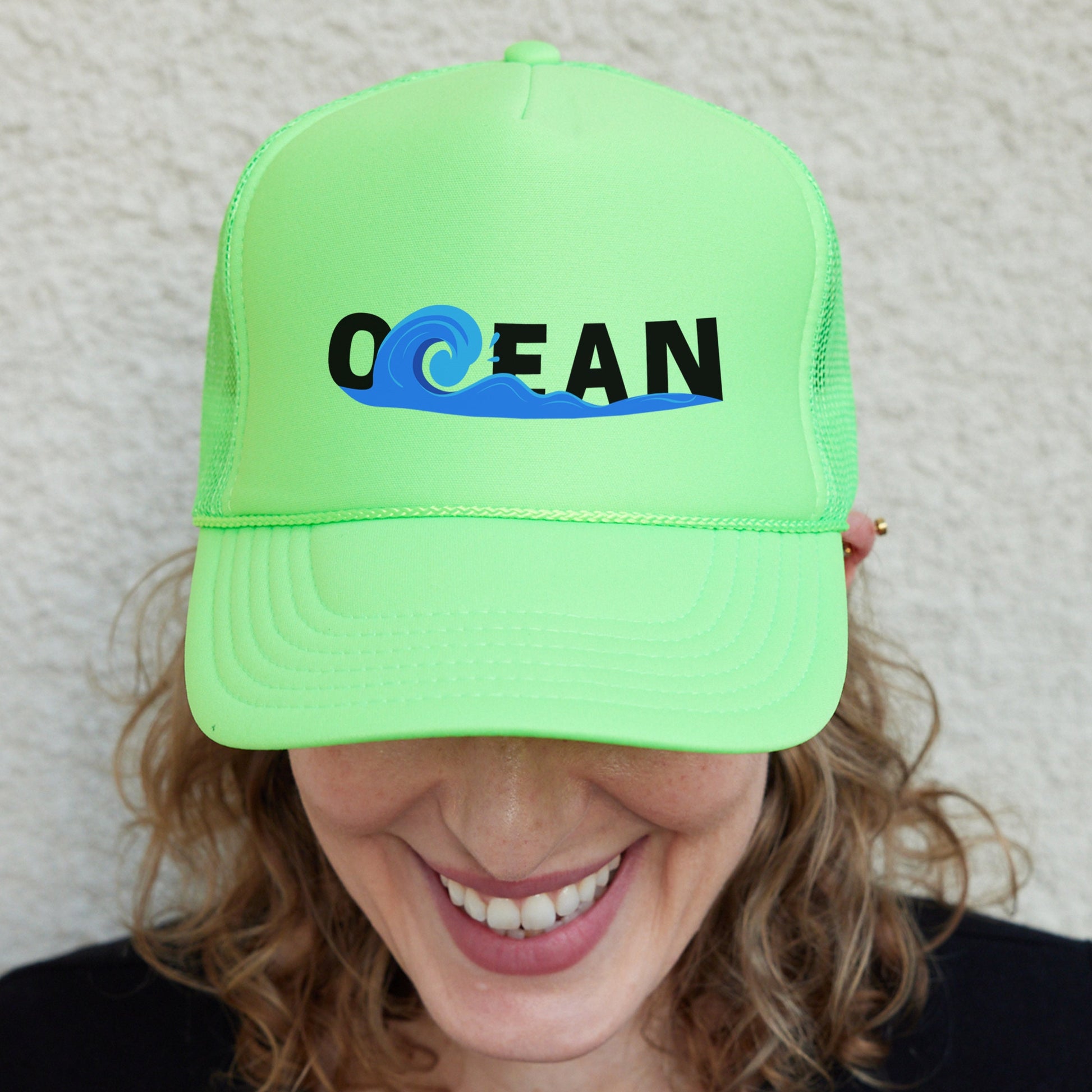 a smiling woman wearing a neon green ocean trucker hat