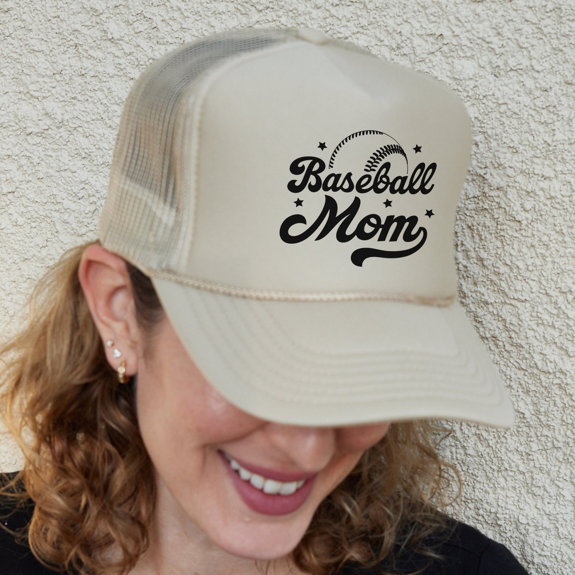 a smiling woman wearing a baseball mom hat