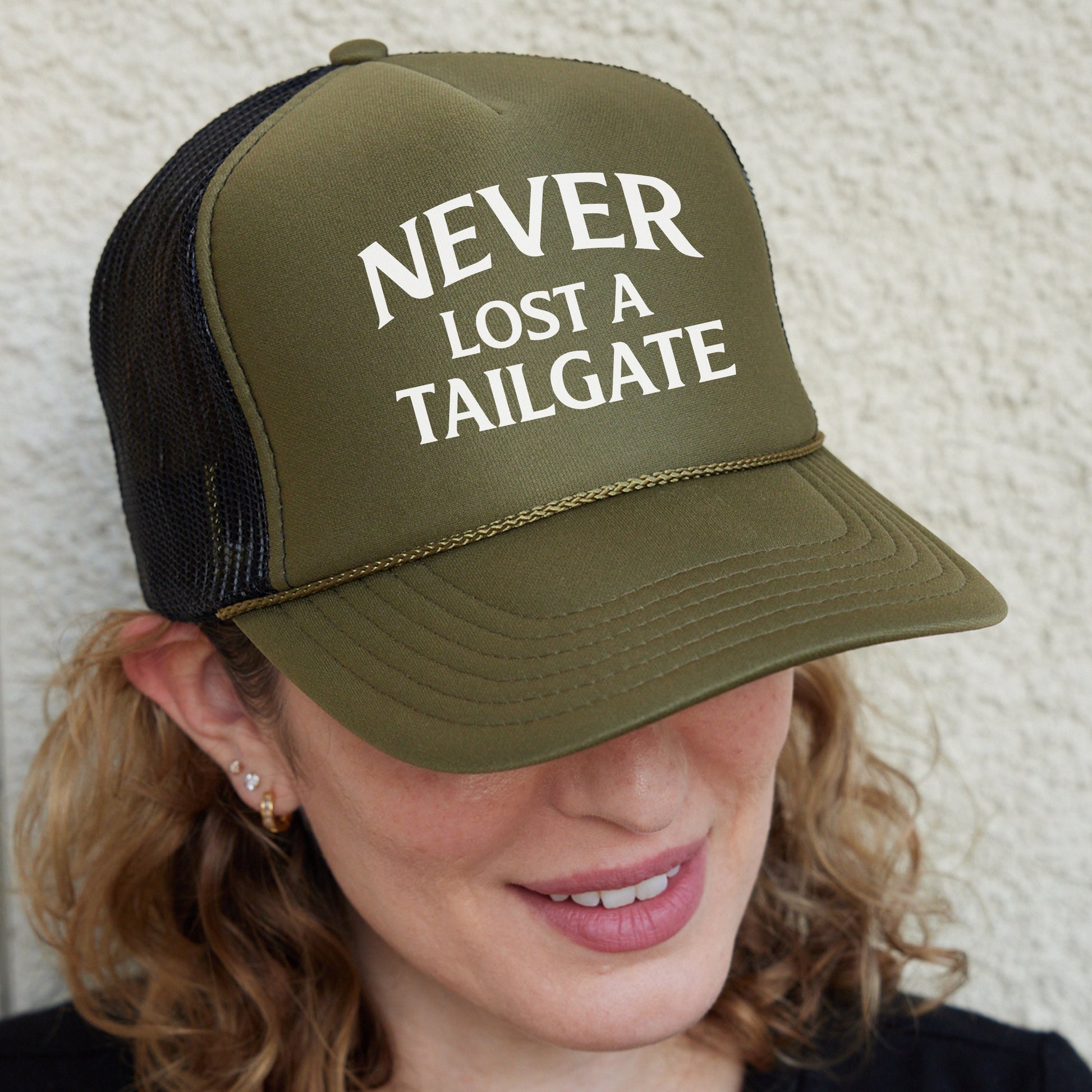 a woman wearing a trucker hat that says never lost a tailgate