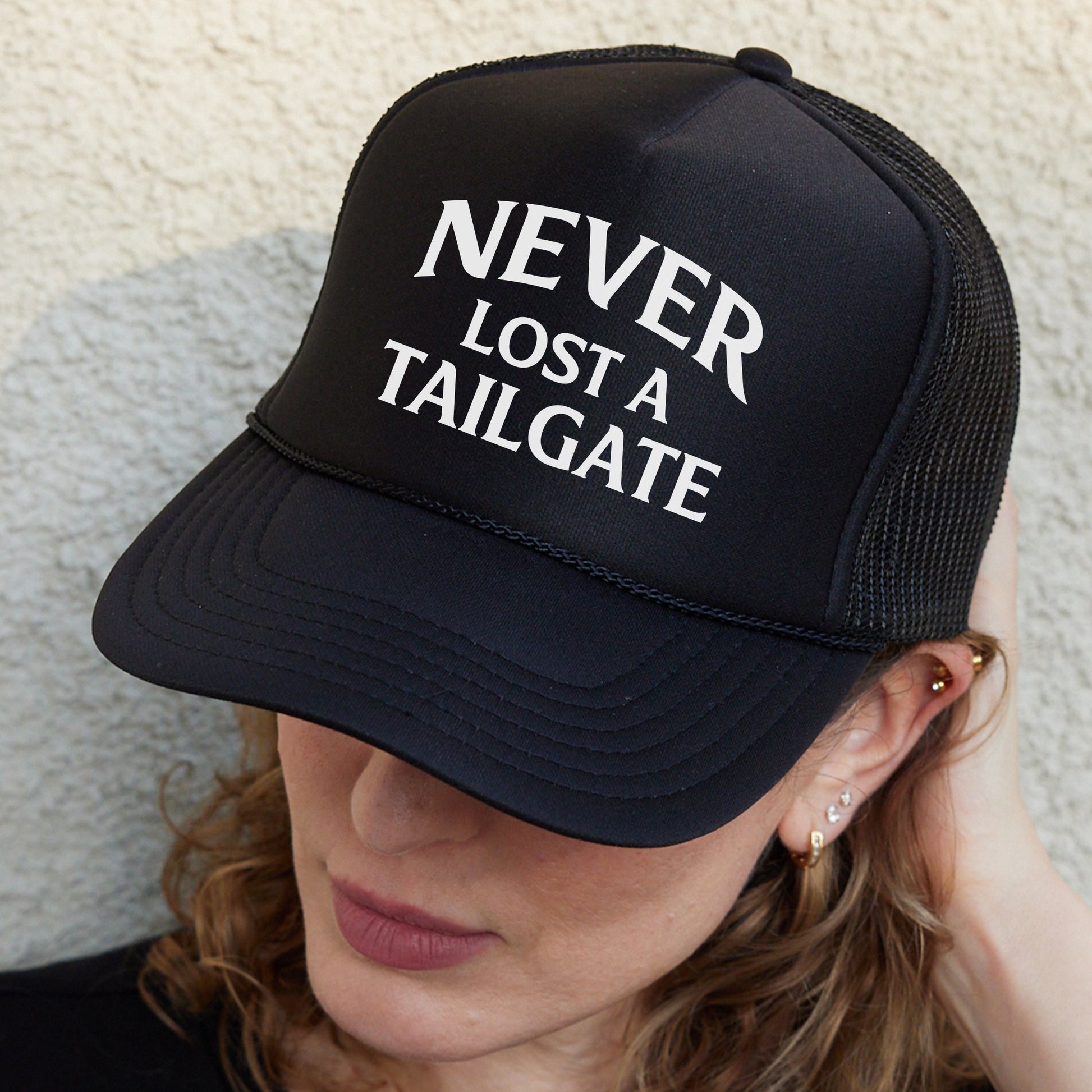 a woman wearing a black trucker hat that says never lost a tailgate