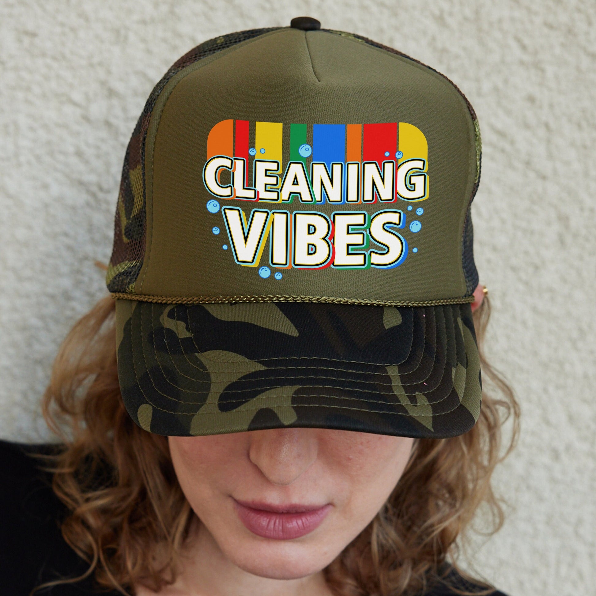 a woman wearing a camo trucker hat with cleaning vibes on it