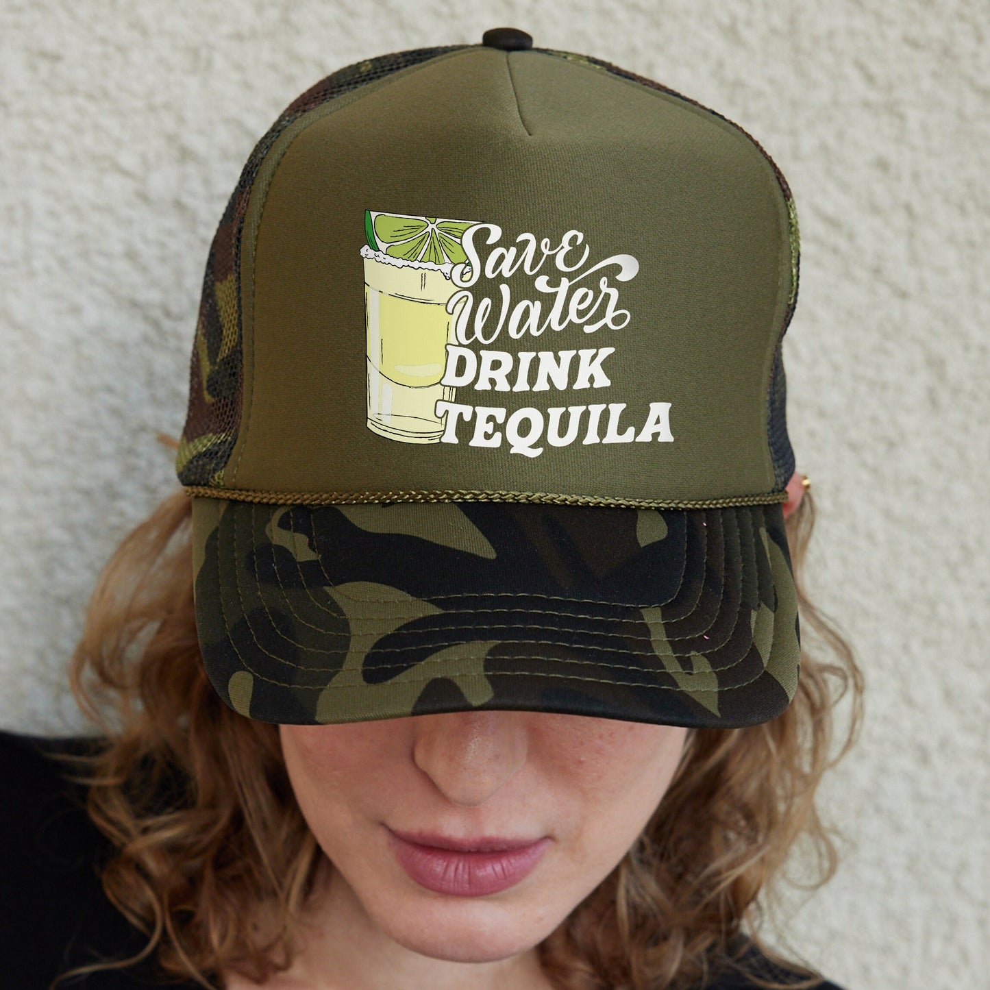 a woman wearing a camo trucker hat with a drink on it