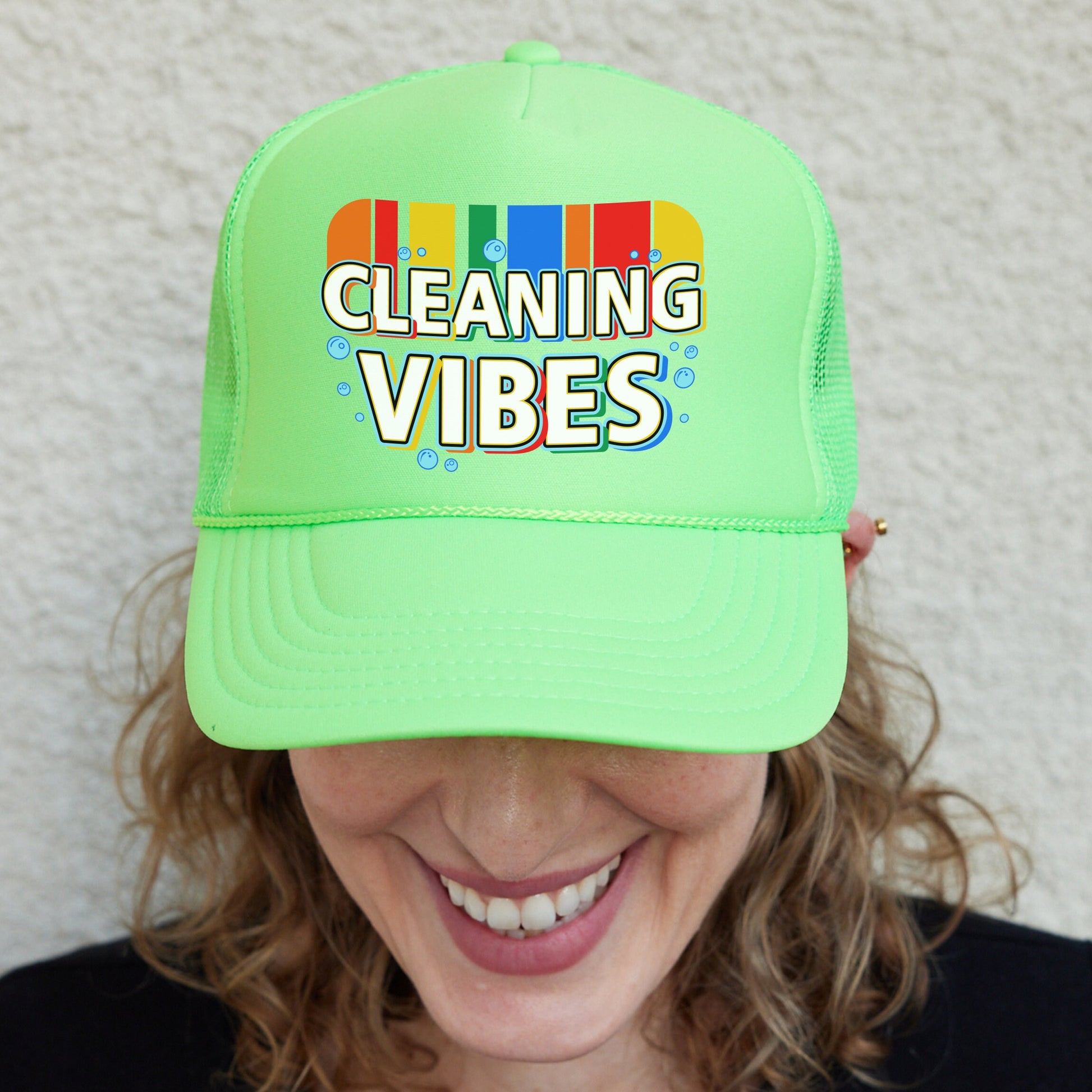 a smiling woman wearing a green cleaning vibes hat