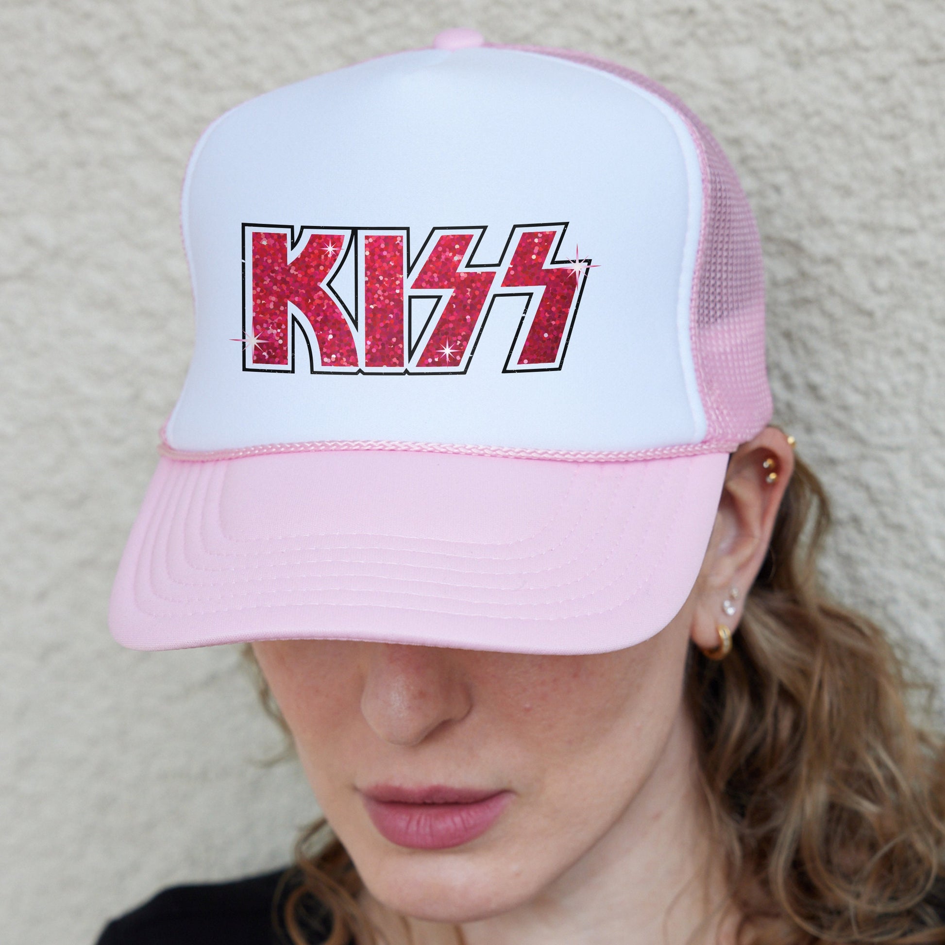 a woman wearing a pink and white kiss trucker hat