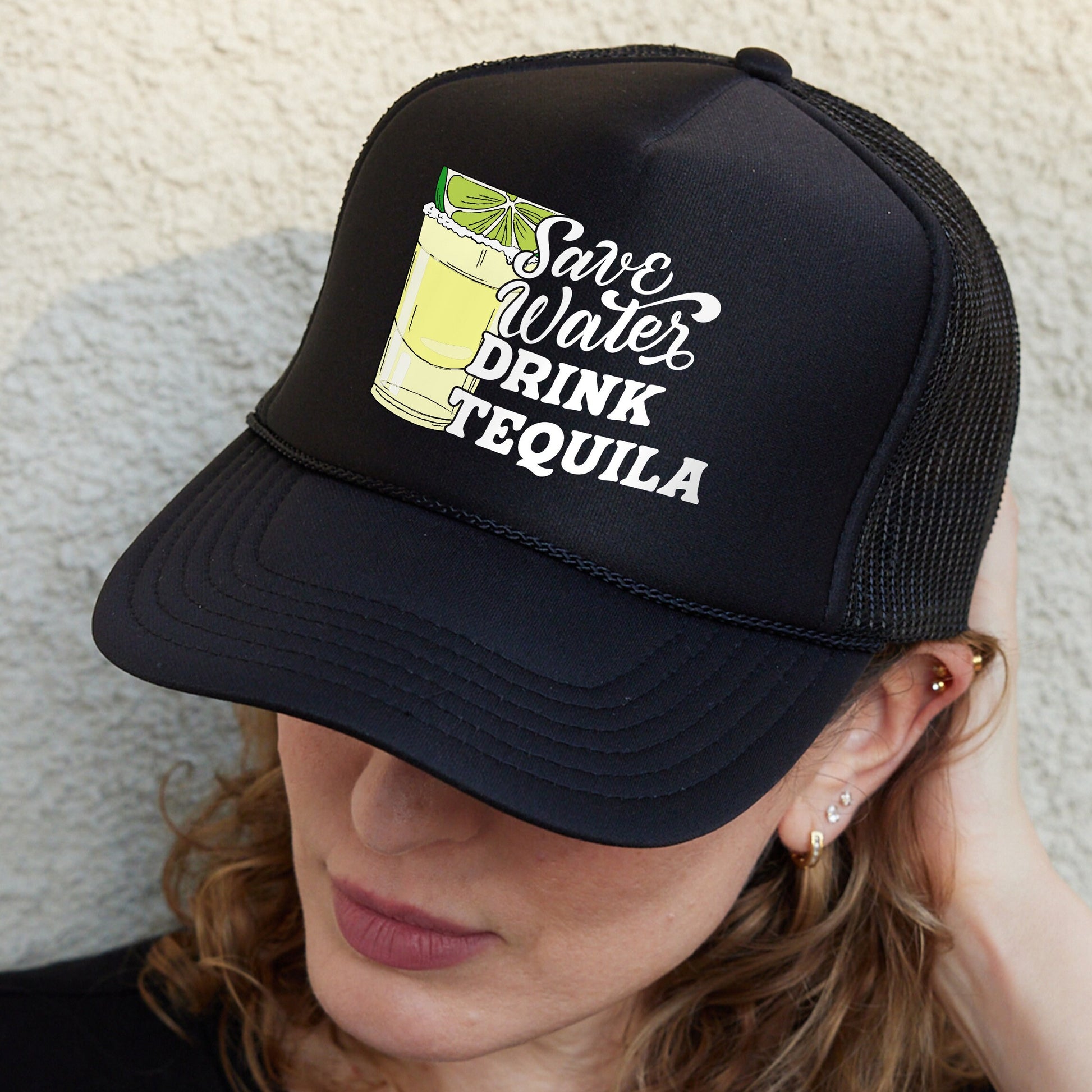 a woman wearing a black trucker hat with a drink on it