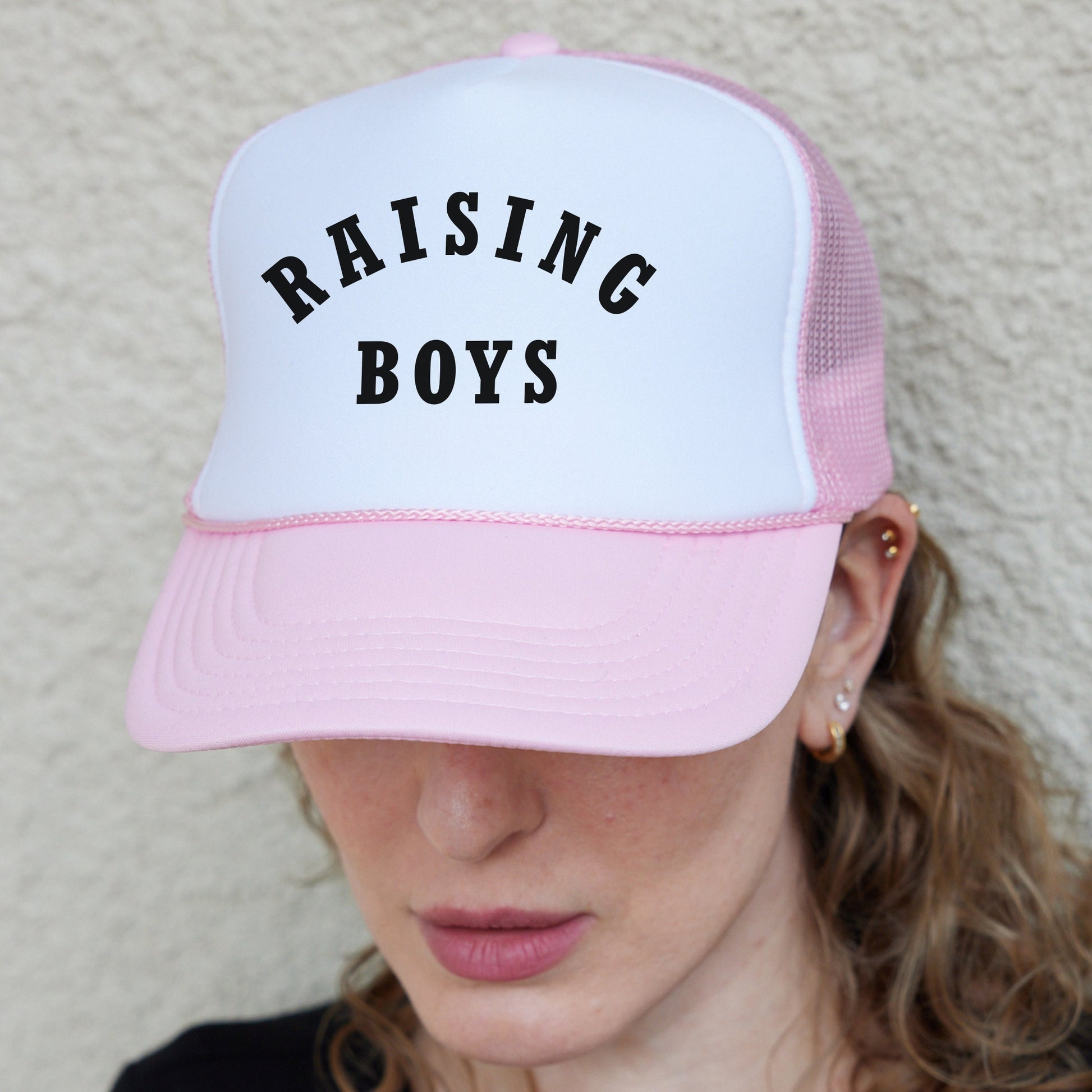 a woman wearing a pink and white hat with the words raising boys on it