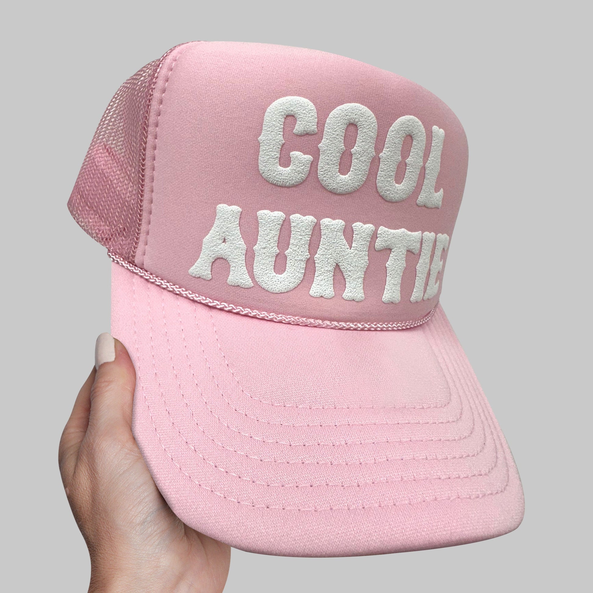 a person holding a pink hat with the words cool aunt on it