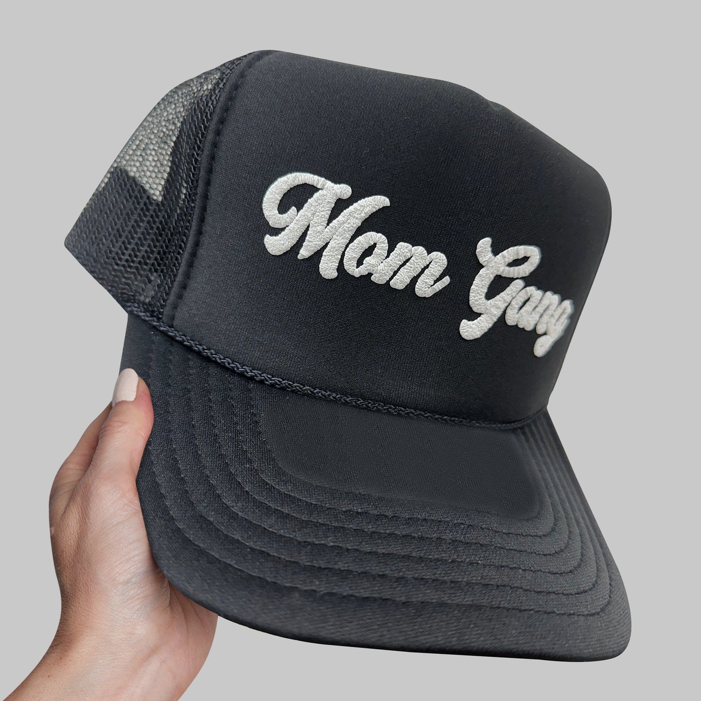 a hand holding a black trucker hat with the word mom gay on it