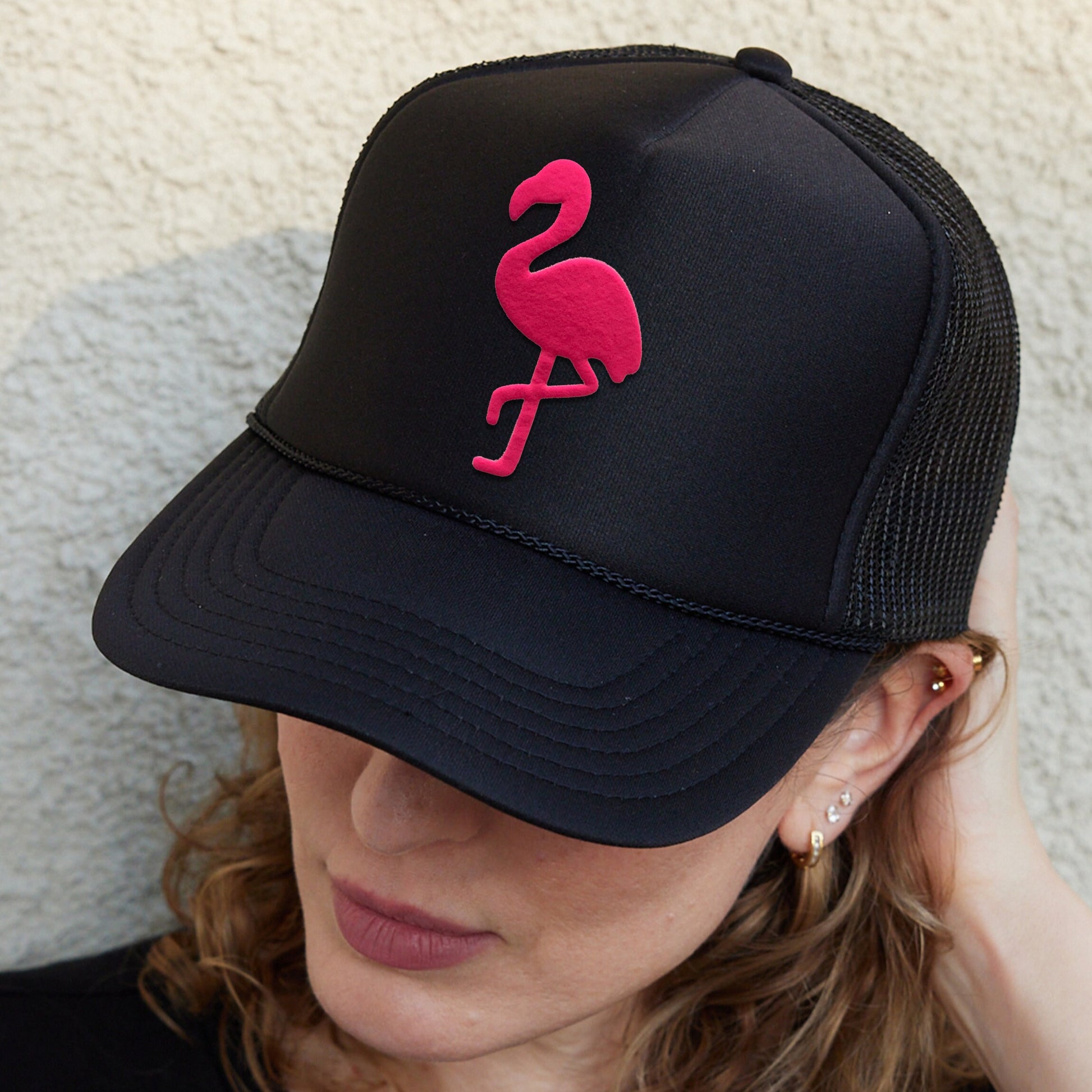 a woman wearing a black hat with a pink flamingo embroidered on it