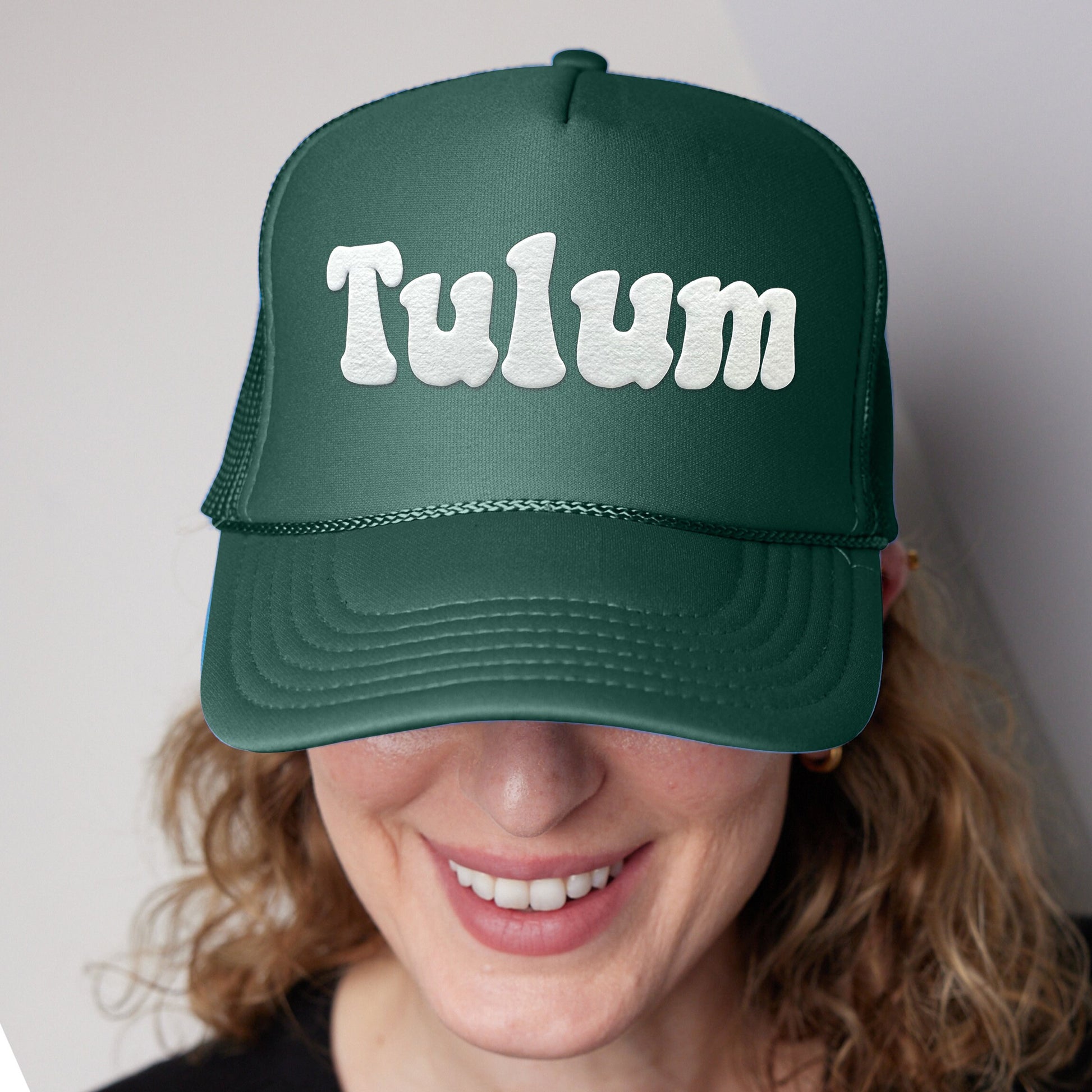 a woman wearing a green trucker hat with the word tulm on it