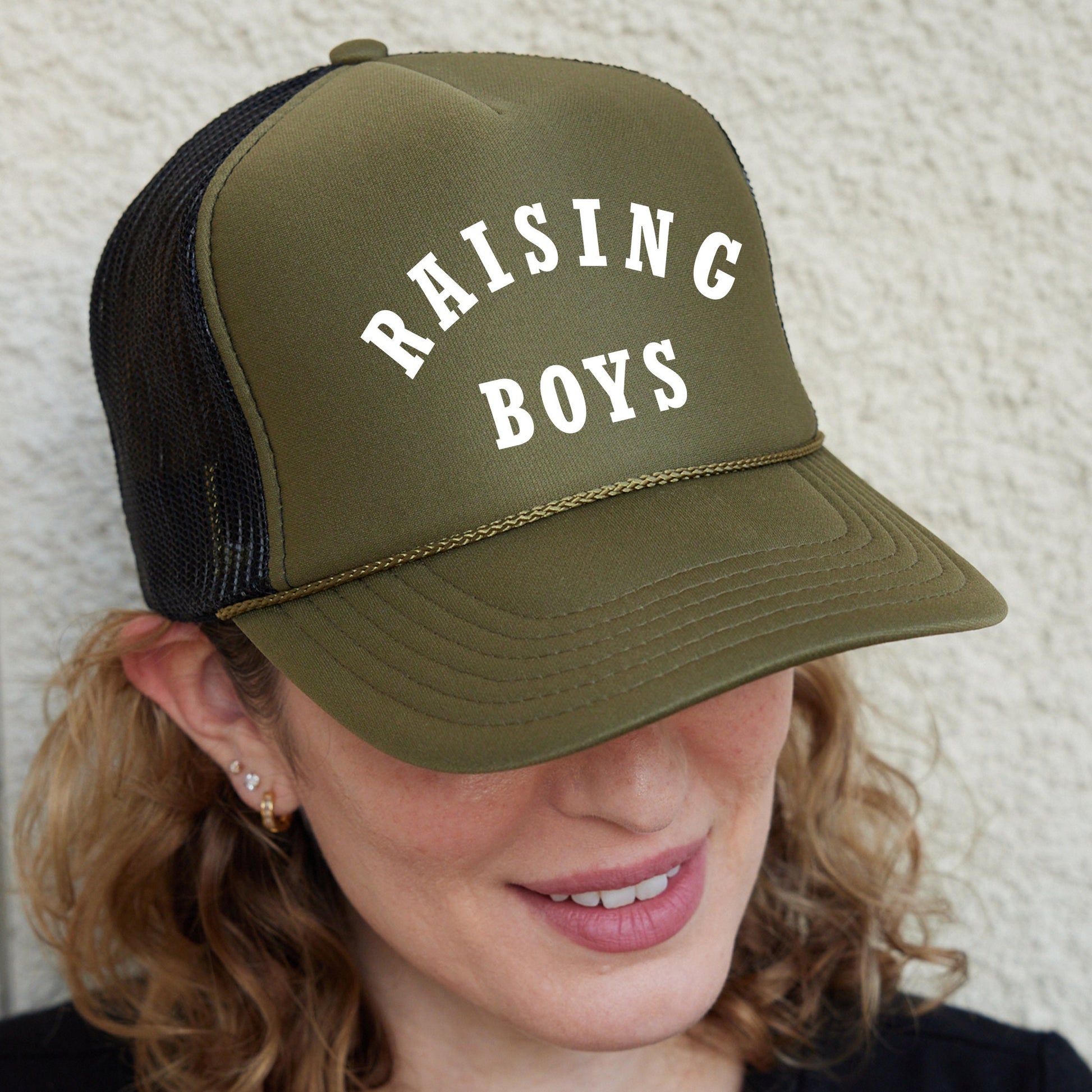 a woman wearing a trucker hat that says raising boys