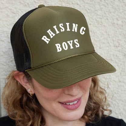 a woman wearing a trucker hat that says raising boys