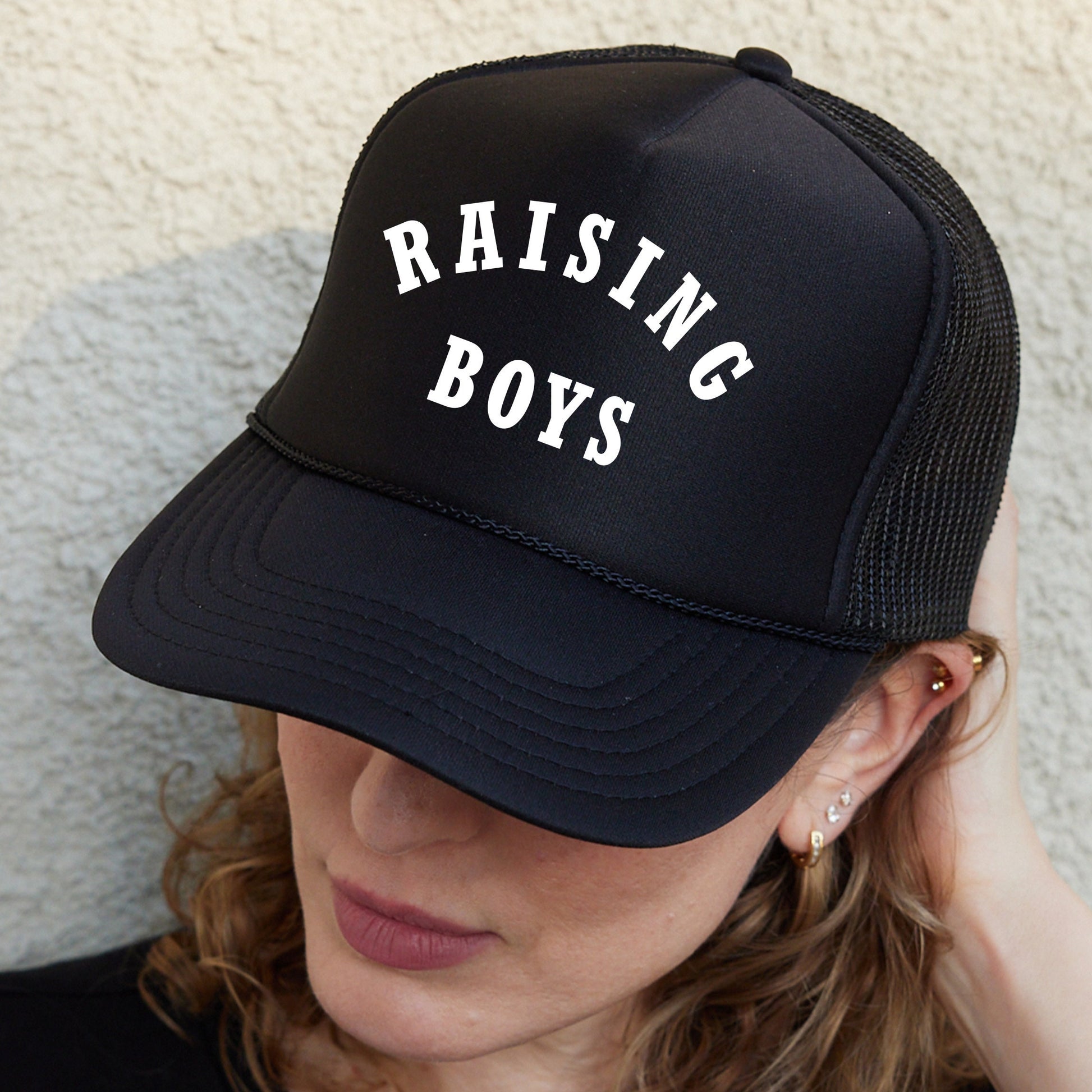 a woman wearing a black hat with the words raising boys on it