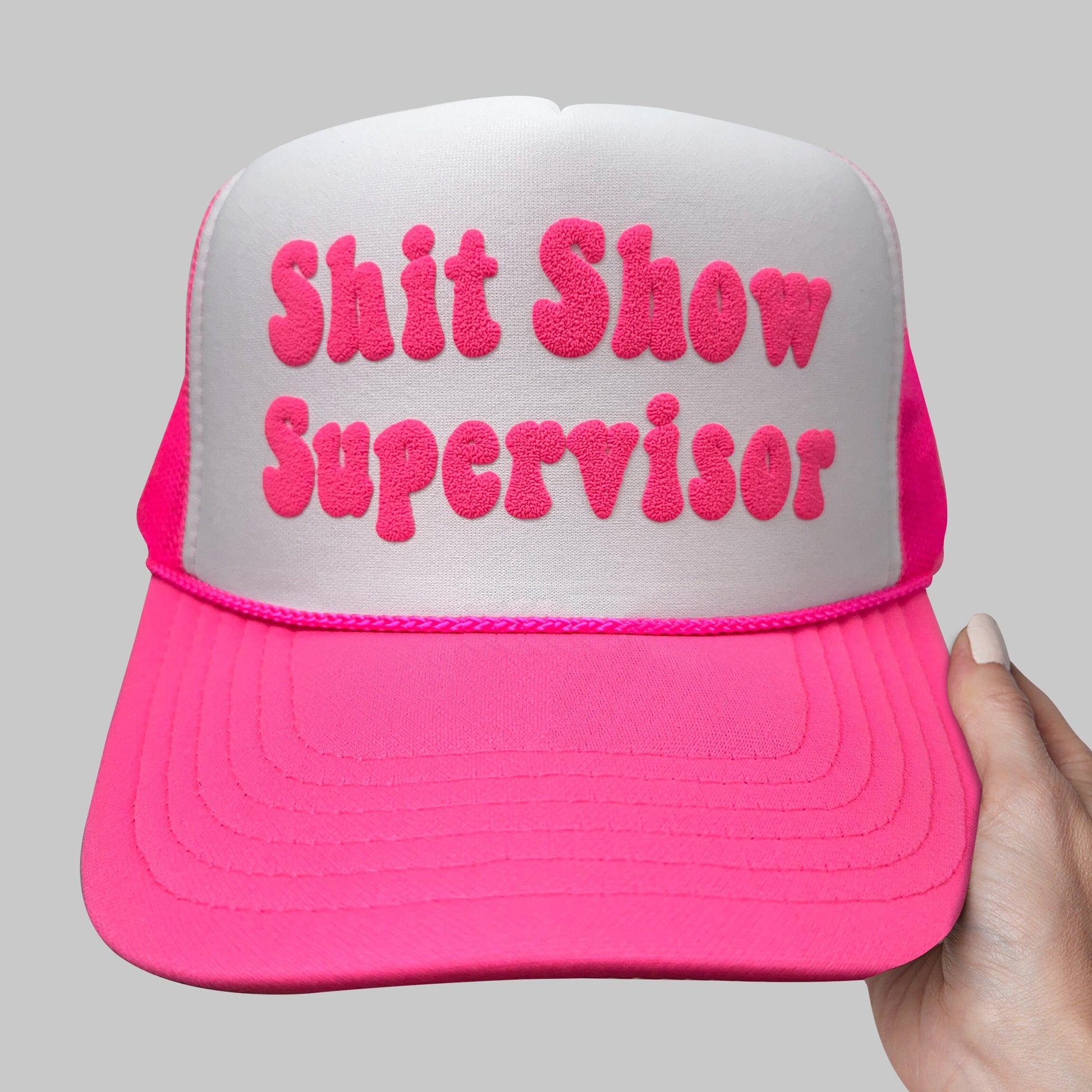 a pink and white hat that says shit show supervisor
