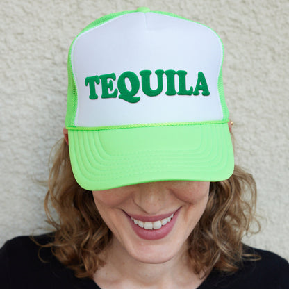 a smiling woman wearing a green and white tequila trucker hat