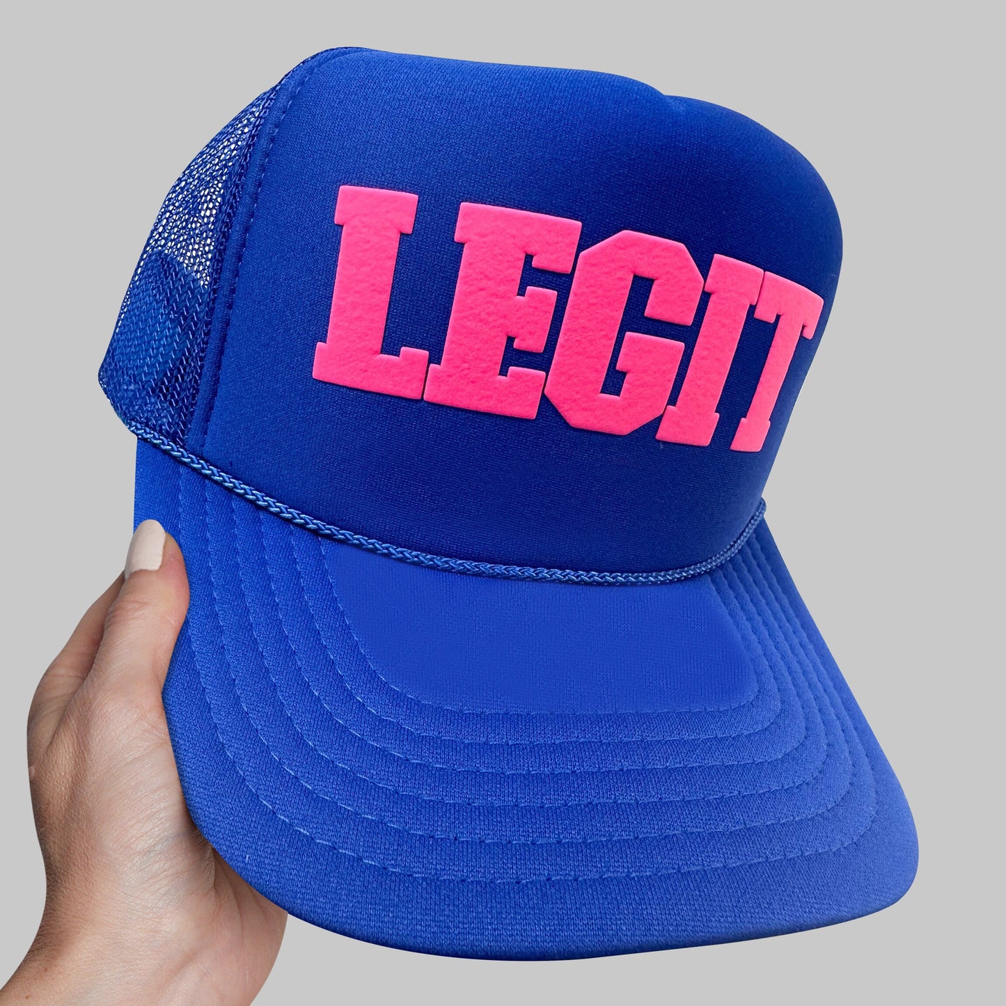 a hand holding a blue and pink hat with the word legit printed on it