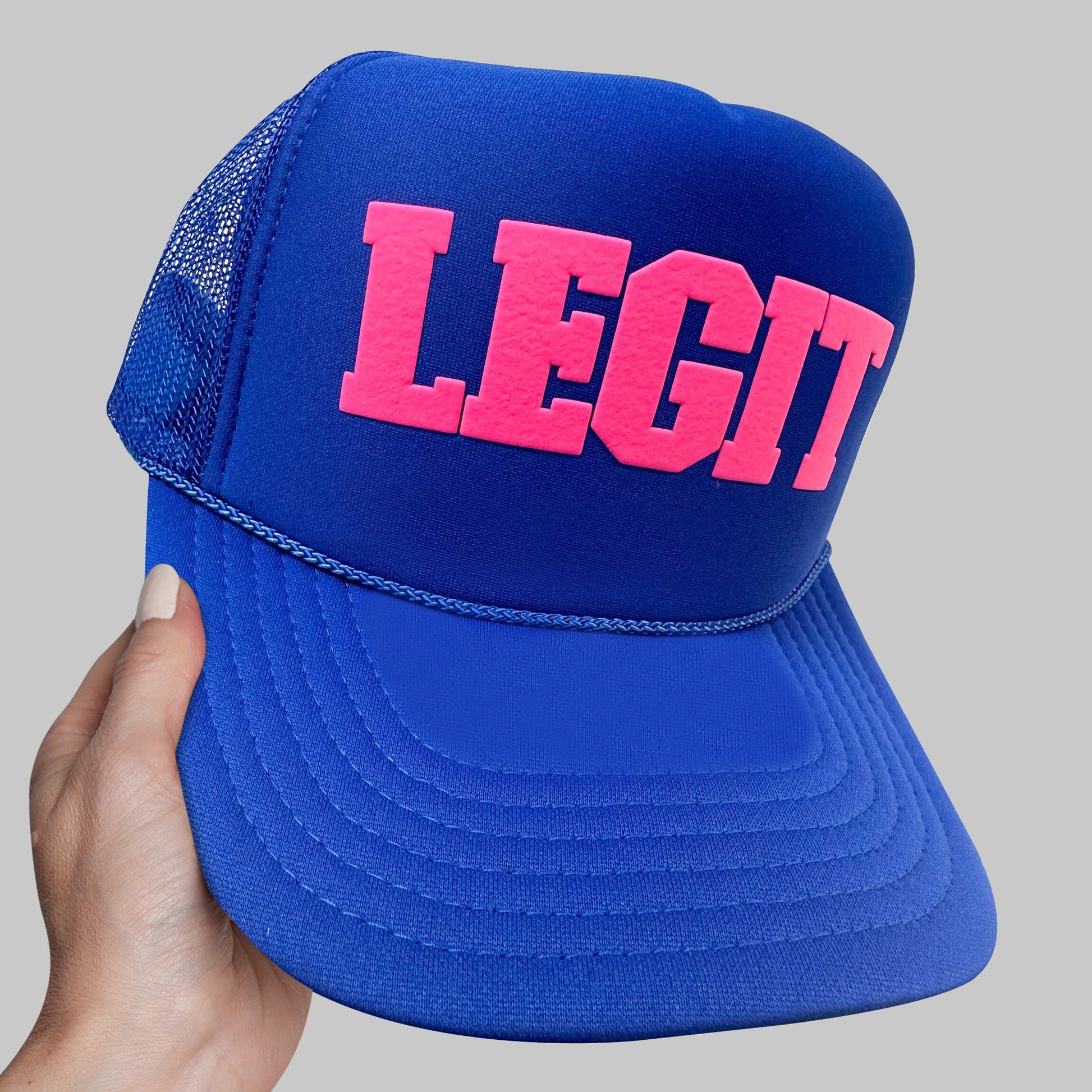 a hand holding a blue and pink hat with the word legit printed on it