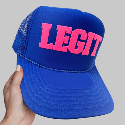 a hand holding a blue and pink hat with the word legit printed on it