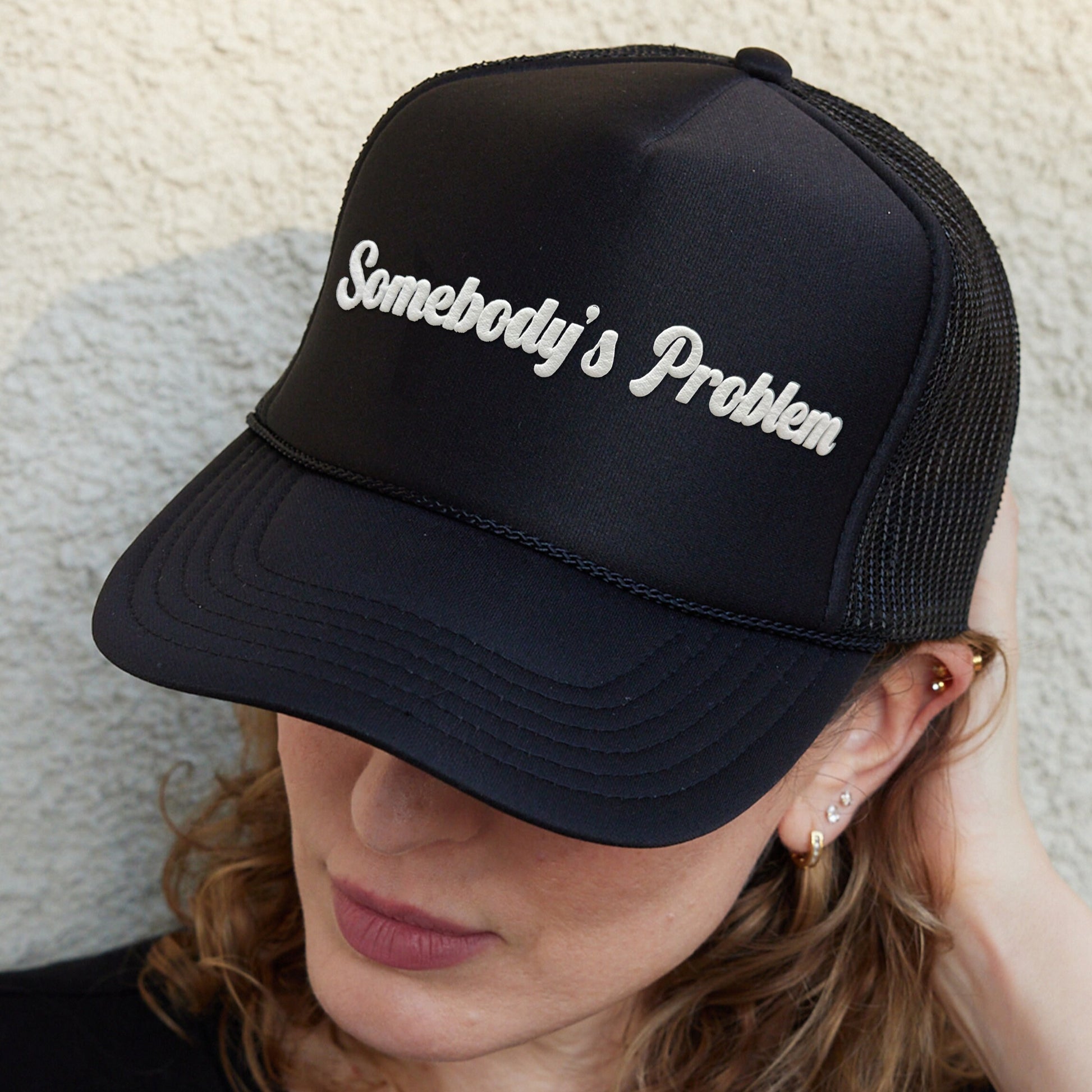 a woman wearing a black hat with somebody&#39;s problem written on it