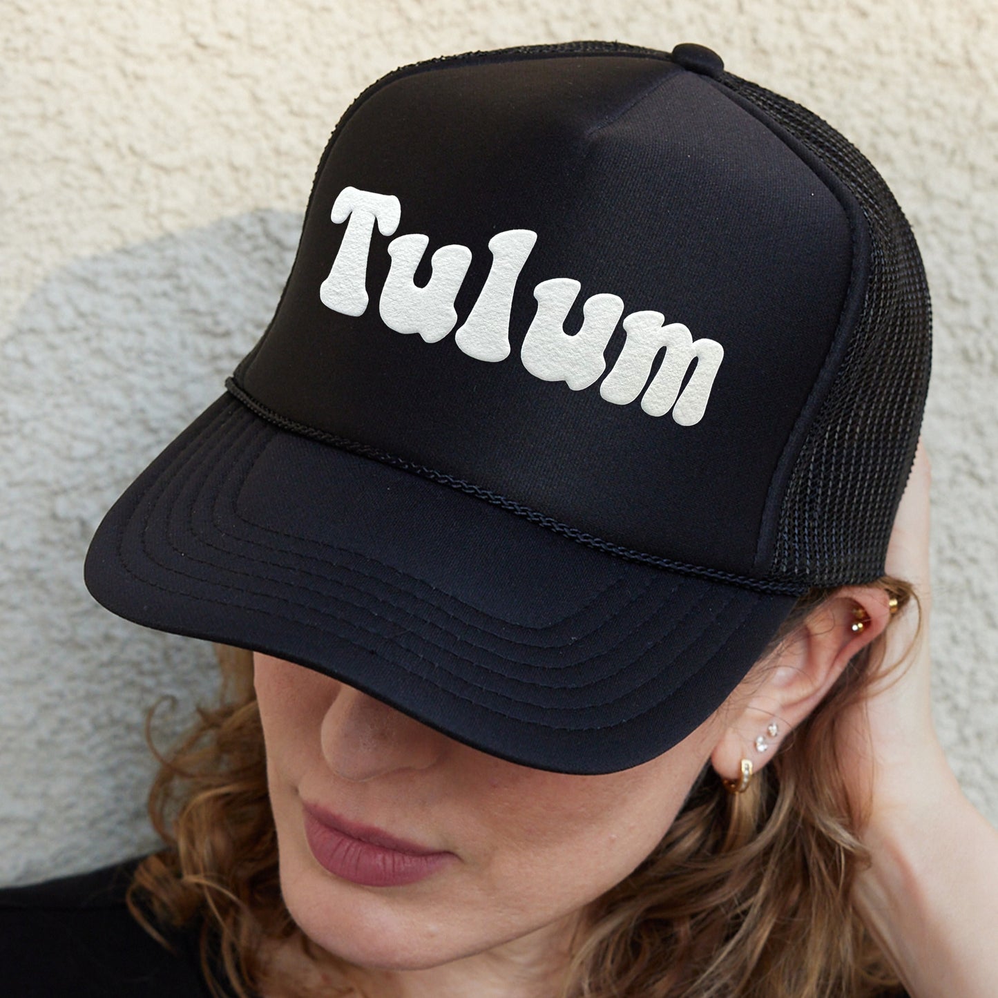a woman wearing a black trucker hat with the word tulm written on it