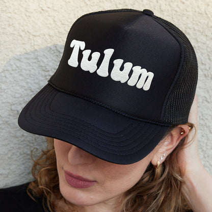 a woman wearing a black trucker hat with the word tulm written on it
